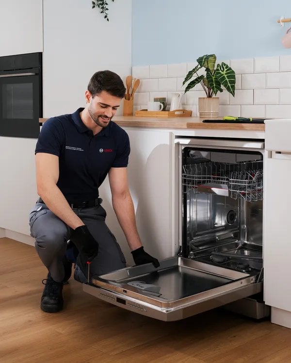 Técnico de servicio instalando o reparando secadora integrada bajo mostrador en cocina blanca
