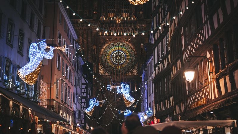 Rue décorée de Noël avec anges illuminés bleus et grande rosace dorée d'une cathédrale en arrière-plan.