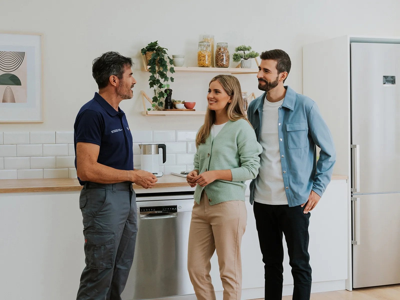 Pareja joven conversando con técnico de servicio en cocina minimalista junto a electrodomésticos